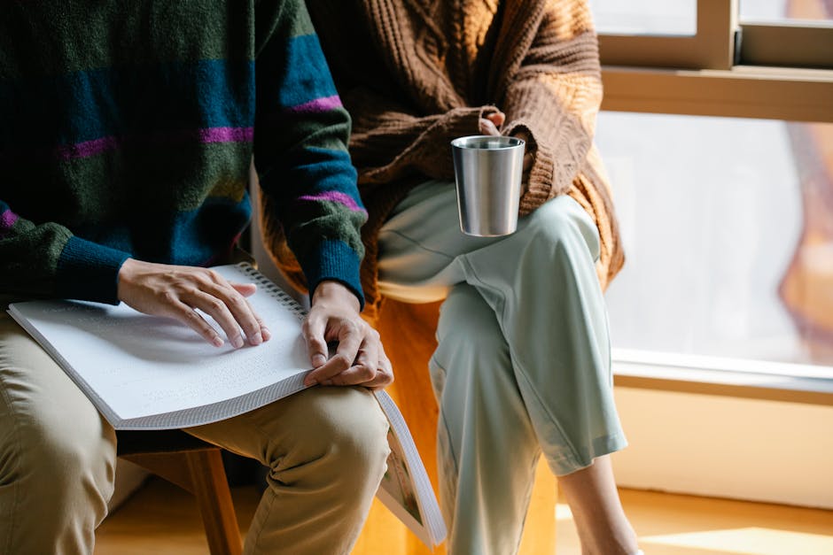 Persona che legge un libro in braille mentre un'altra persona beve, imparando a chiedere aiuto in spagnolo.