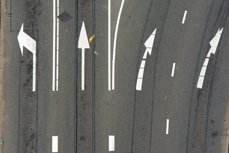 Vista aerea di segnaletica orizzontale stradale: frecce direzionali e linee continue, elementi per la mobilità e l'orientamento nel contesto urbano.