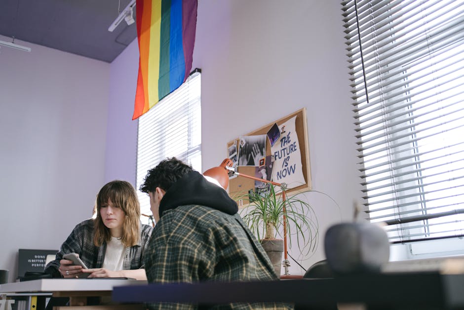 Giovani professionisti collaborano in ufficio moderno con bandiera LGBTQ+, simbolo di inclusione e futuro sostenibile nell'offerta aziendale.
