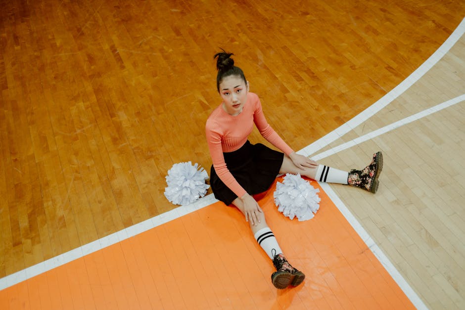 Giovane cheerleader seduta sul campo da basket con pon pon, preparazione fisica per affrontare le prove del concorso scuola 2025
