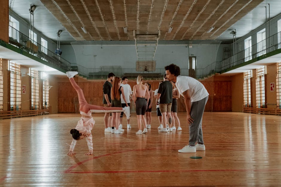 Ragazza esegue verticale in palestra con istruttore e gruppo. Vigilanza e sicurezza nelle attività sportive scolastiche.