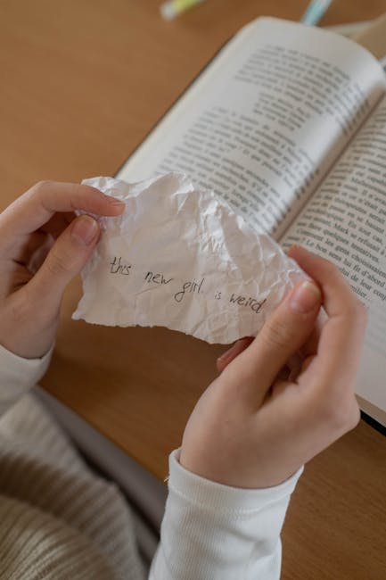 Biglietto con scritta 'questa nuova ragazza è strana' in mano a studente, possibile riferimento a bullismo scolastico