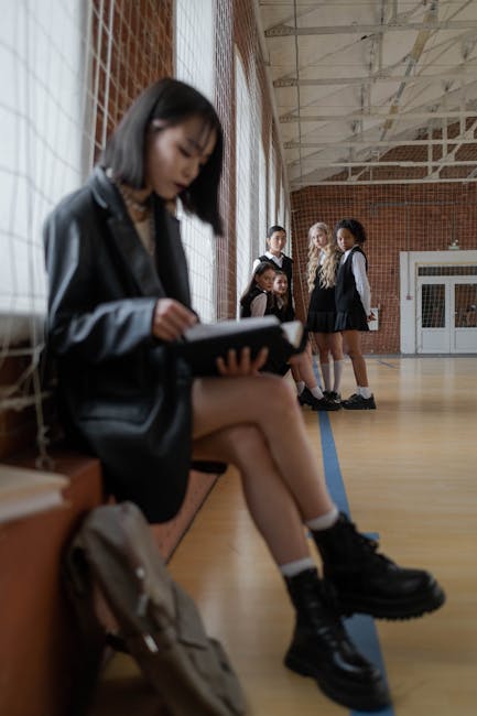 Studentessa legge in palestra con compagne sullo sfondo. Inclusione scolastica e diversità per un'istruzione equa e accessibile.