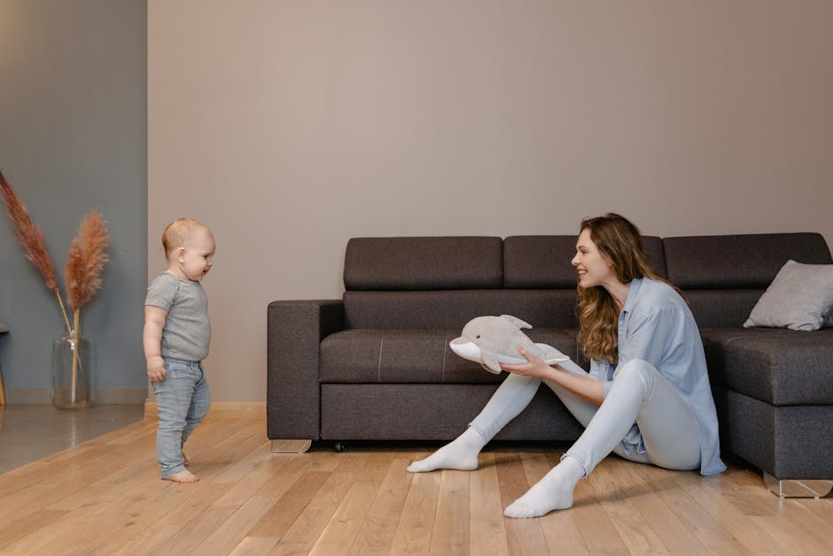 Madre sorridente con peluche a forma di delfino interagisce con il suo bambino in un ambiente domestico accogliente e luminoso. Genitorialità e infanzia.
