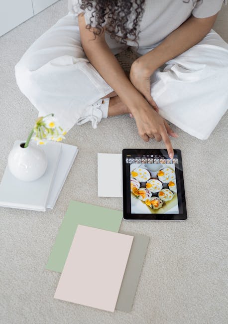 Ragazza seduta sul pavimento che guarda foto di muffin su un tablet, con fiori e campioni di colore intorno.