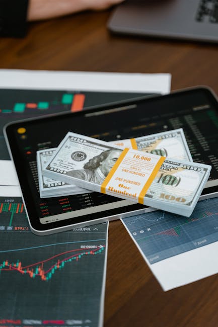 Pacchi di banconote da 100 dollari su tablet con grafici finanziari, iniziativa libri per famiglie a basso reddito