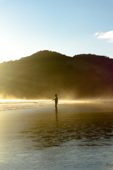 Uomo solitario pesca all'alba su spiaggia nebbiosa, immagine evocativa della solitudine in 100 Anni di Solitudine di Garcia Marquez.
