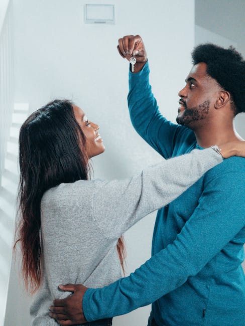 Giovane coppia afroamericana celebra l'acquisto della casa nuova, mostrando le chiavi, simbolo di un futuro condiviso e relazioni interpersonali positive.