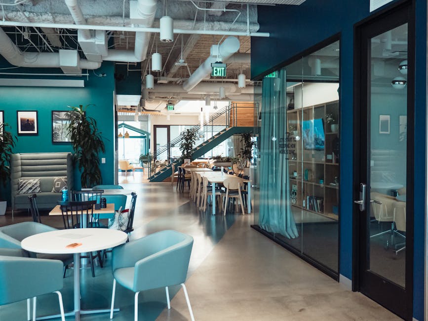 Interno ufficio moderno con tavoli e sedie regolabili per ergonomia e benessere dei dipendenti, design open space e illuminazione naturale.