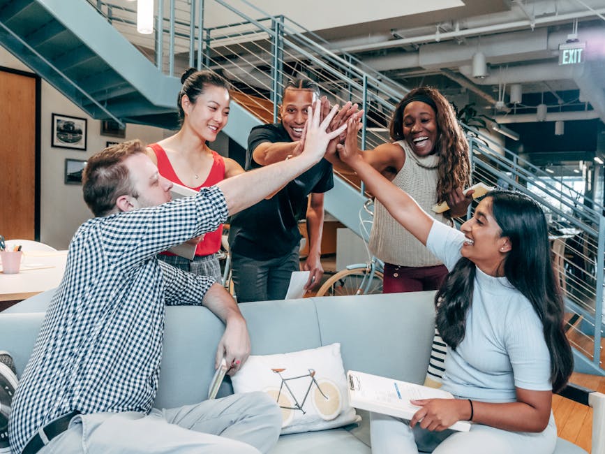 Gruppo di studenti universitari multietnici che celebrano un successo formativo con un high five in un ambiente di co-working aziendale