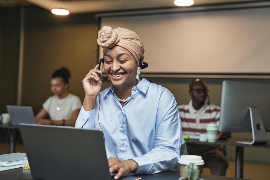 Donna sorridente con cuffie lavora al computer, promuovendo comunicazione inclusiva e responsabile in ufficio moderno