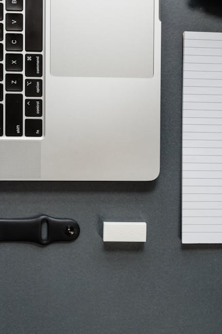 Strumenti virtuali per la produttività: laptop, blocco note, smart watch e gomma su sfondo scuro, focus sull'organizzazione e l'efficienza.
