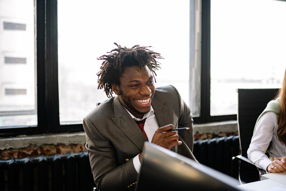 Uomo sorridente in giacca e cravatta durante una riunione, simbolo di relazioni positive tra colleghi e ambiente di lavoro sereno.