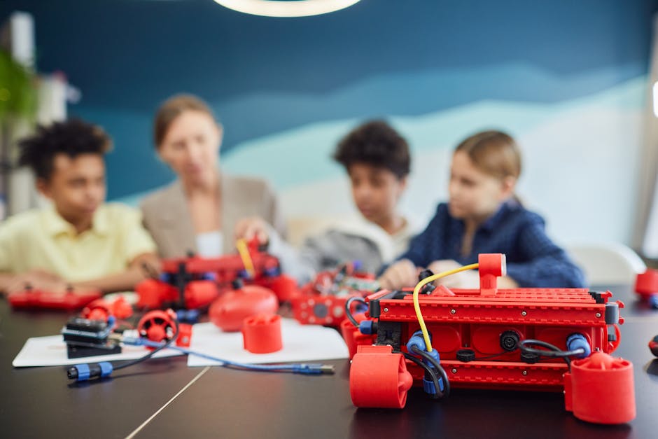 Bambini che partecipano a un laboratorio di coding avanzato, costruendo robot con componenti rossi sotto la guida di un'insegnante