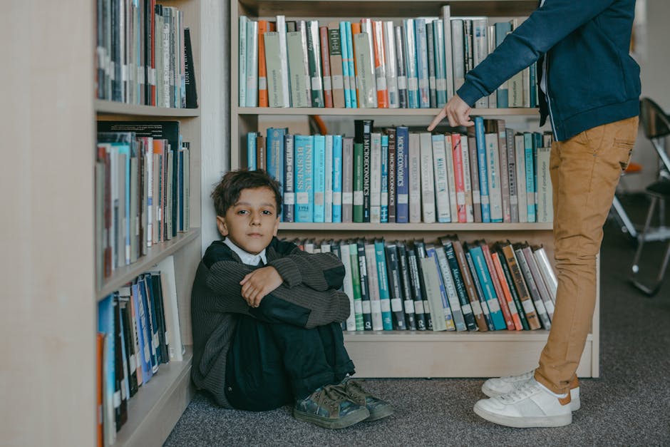 Ragazzo seduto in biblioteca con un adulto che indica un libro, metafora del ritorno sui libri e dell'importanza della conoscenza