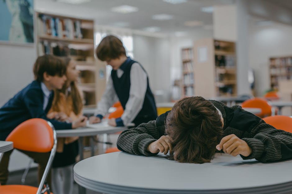 Adolescente con la testa sul tavolo a scuola, simbolo di stress e problemi di salute mentale giovanile in Italia, tra coetanei