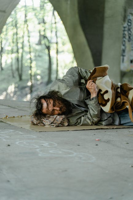 Uomo senzatetto dorme sotto un ponte in Calabria, simbolo di povertà ed esclusione sociale nella regione italiana.