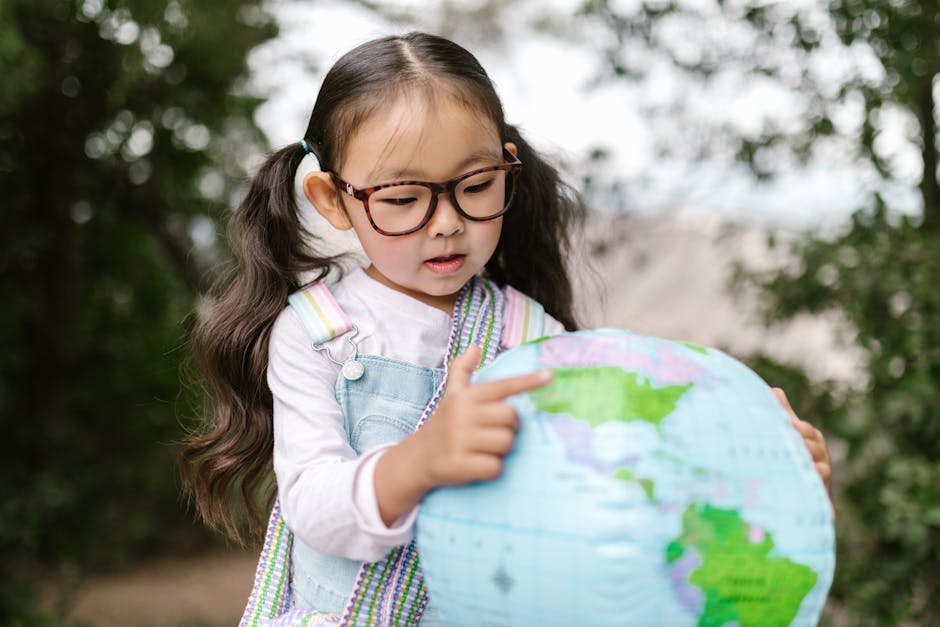 Bambina asiatica con occhiali che indica un mappamondo gonfiabile, attività di educazione interculturale e scoperta del mondo