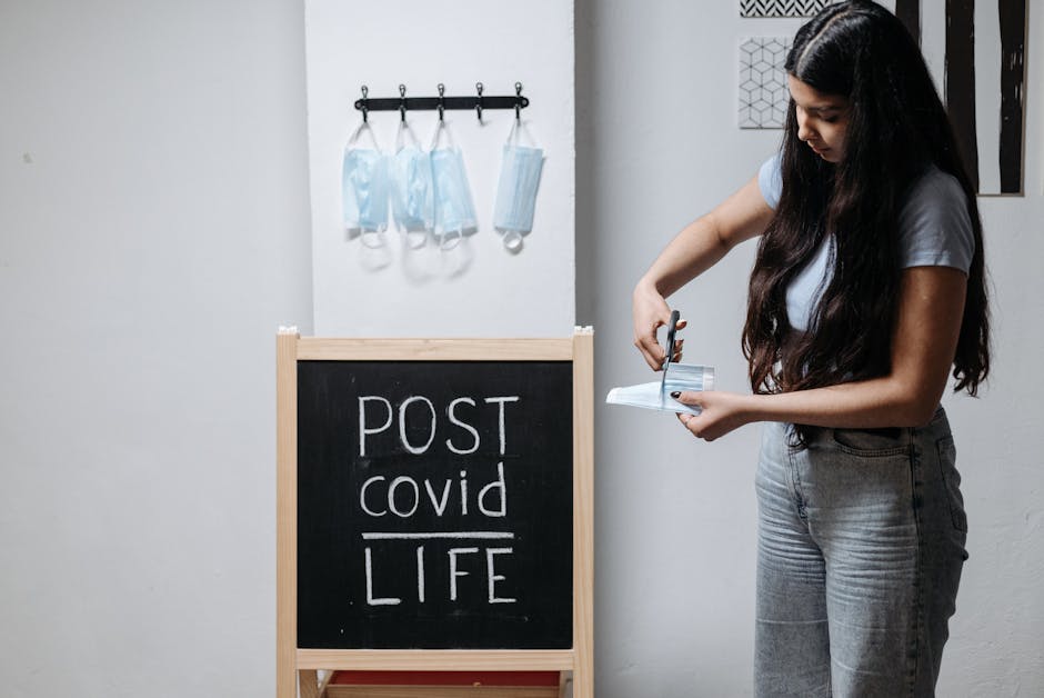 Donna che taglia una mascherina chirurgica di fronte a una lavagna con scritto Post Covid Life, simbolo di adattamento e cambiamento