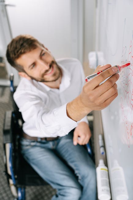 Uomo in sedia a rotelle che scrive su lavagna bianca, esempio di didattica inclusiva e accessibilità per tutti gli studenti.
