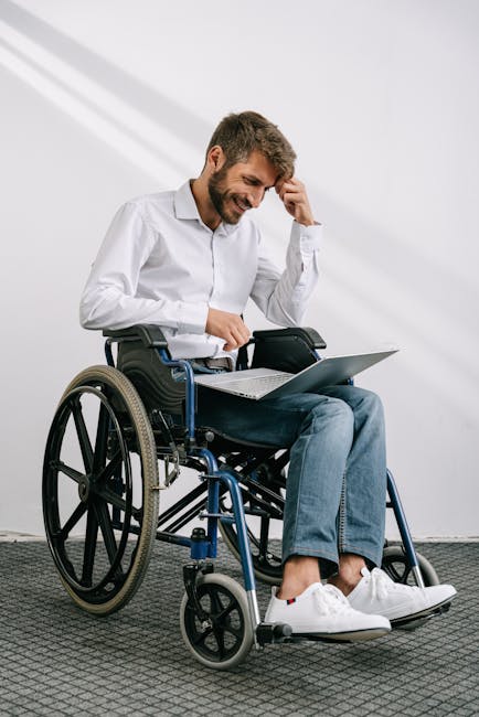 Uomo sorridente su sedia a rotelle che usa un laptop, esempio di adattamento ragionevole per l'inclusione lavorativa e il successo professionale.