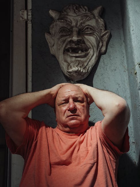 Uomo con le mani sulla testa sotto una maschera demoniaca, simbolo di ansia latente e pressione psicologica nell'articolo.