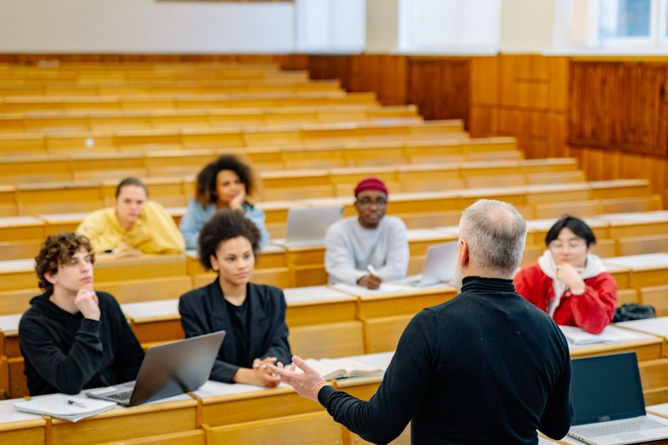 Docente in aula che spiega gli organi collegiali di classe e intersezione, con studenti che prendono appunti e seguono la lezione.