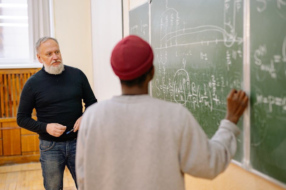 Studente al Politecnico di Milano scrive equazioni alla lavagna sotto lo sguardo attento di un professore durante la lezione