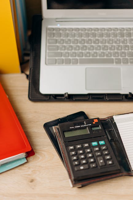 Calcolatrice, quaderno e laptop su scrivania per calcolo area rettangolo e applicazioni pratiche, strumenti di lavoro e studio.