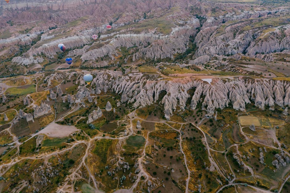 Vista aerea mozzafiato della Cappadocia con formazioni rocciose uniche e mongolfiere colorate che solcano il cielo all'alba.