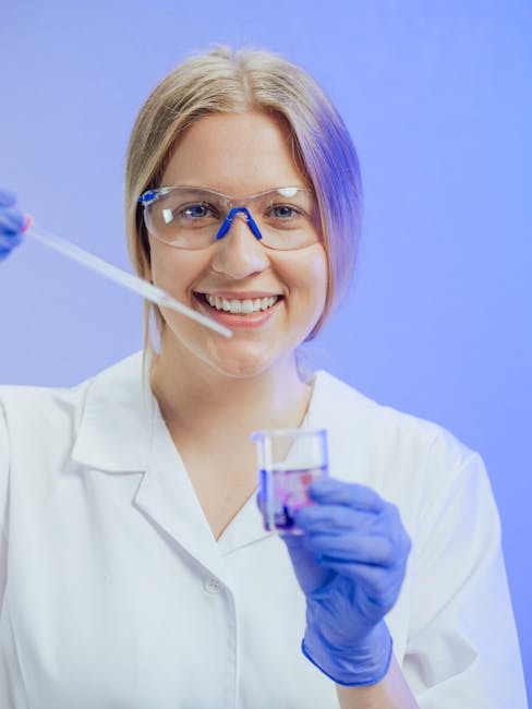 Giovane chimica sorridente esegue analisi in laboratorio di chimica analitica con provetta e beuta, indossa camice e occhiali protettivi.