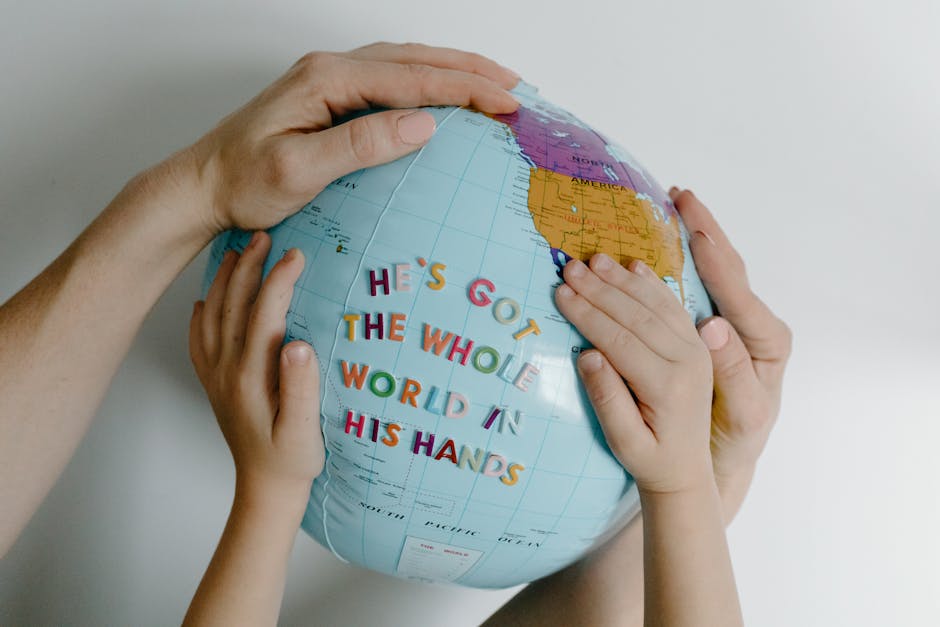 Mani di adulto e bambino che tengono un mappamondo gonfiabile con la scritta He's got the whole world in his hands