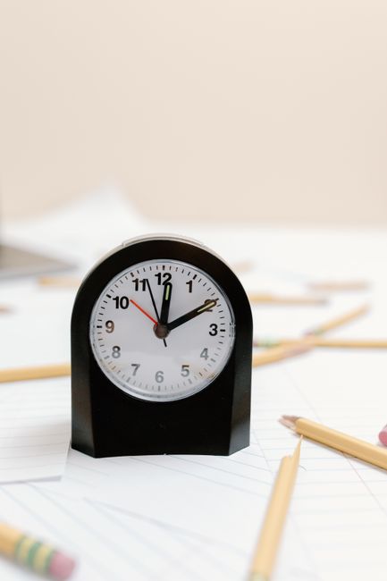 Orologio da scrivania nero su fogli a righe con matite sparse, simboleggia le scadenze per la valutazione dei dirigenti scolastici