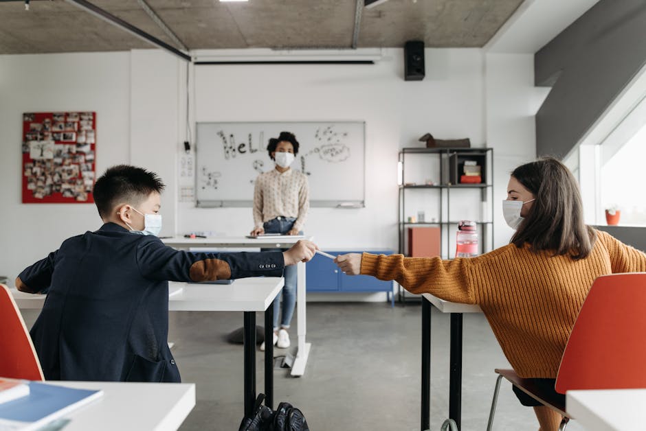 Inclusione scolastica: studenti con mascherina si passano una penna in classe, insegnante sullo sfondo. Percorso inclusivo per alunni con disabilità.