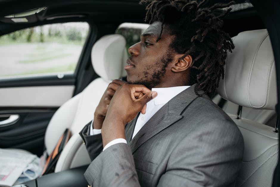 Uomo d'affari in auto che si sistema la camicia, simbolo di preparazione e continuità nel successo professionale moderno.