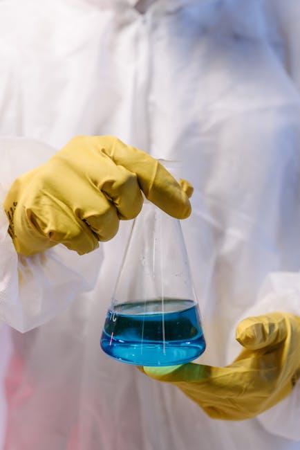 Esercizio di analisi chimica: scienziato con guanti gialli che tiene beuta con liquido blu, parte di esperimento di laboratorio.