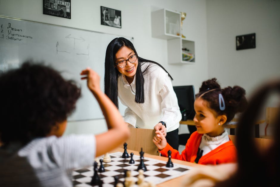 Insegnante asiatica sorridente guida due bambine di etnie diverse durante una partita a scacchi, esempio di didattica differenziata inclusiva.