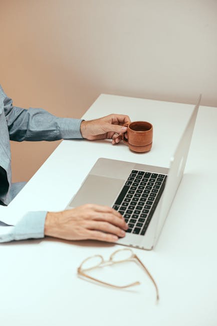 Uomo che lavora al computer con tazza di caffè e occhiali, simbolo di flessibilità organizzativa e didattica moderna
