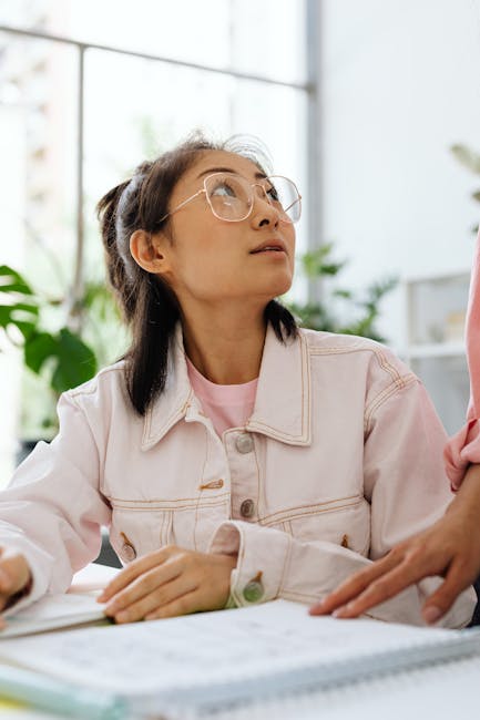 Studentessa asiatica con occhiali guarda in alto, riflettendo sulle opportunità del PNRR per l'istruzione e l'approfondimento.