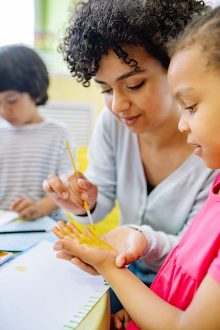 Insegnante dipinge la mano di una bambina con pittura gialla in classe. Immagine per articolo su vita da insegnante e scuola