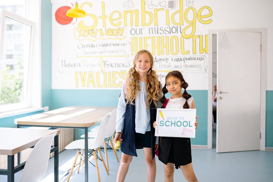 Due studentesse sorridenti in aula con cartello 'Back to School', ambiente scolastico inclusivo e accogliente per l'apprendimento.