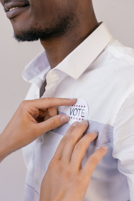 Uomo appunta adesivo VOTE sulla camicia bianca: impegno per il cambiamento e lotta alla violenza contro le donne.
