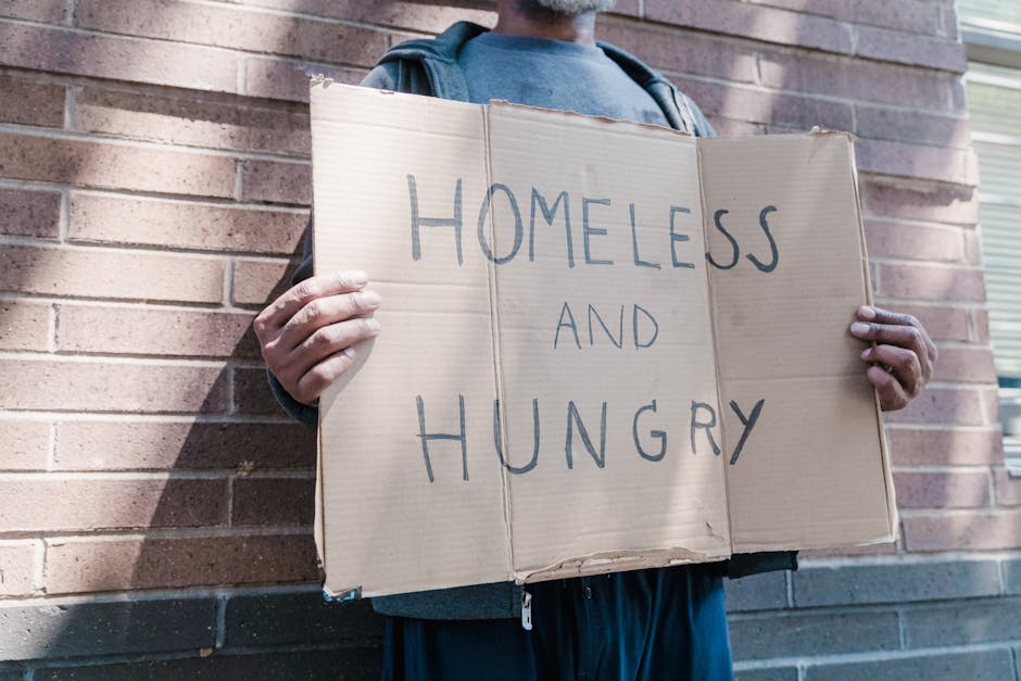 Uomo senzatetto con cartello 'Homeless and Hungry', simbolo della mancanza di percorsi abilitanti e del fabbisogno insoddisfatto.
