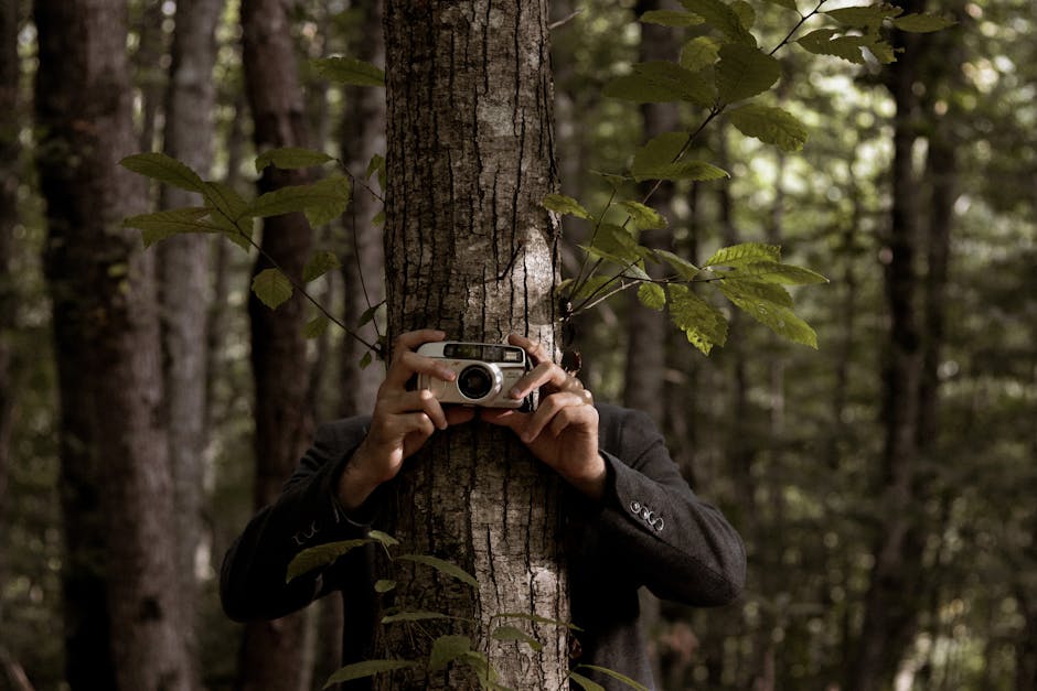 Fotografo nascosto dietro un albero a Sant'Aspino Scafati con macchina fotografica vintage, esplorando la bellezza naturale della Campania.