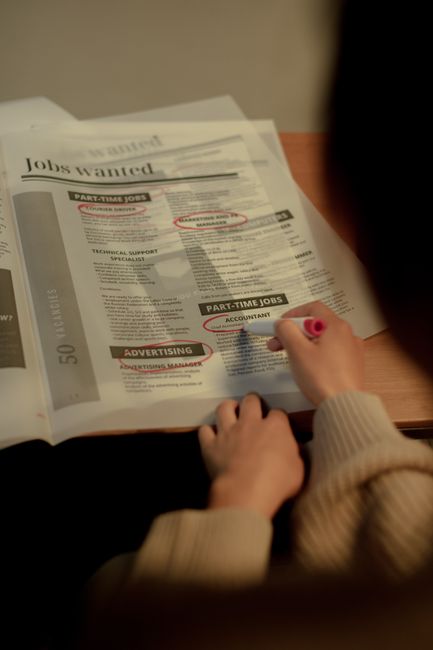 Persona che cerca annunci di lavoro su un giornale, evidenziando posizioni come contabile e manager marketing, in relazione ai 30 CFU ex art. 13