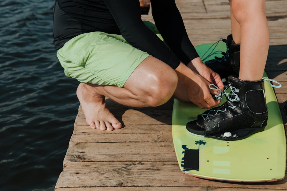 Ragazzo che allaccia gli scarponi da wakeboard su una tavola verde, attività sportiva extrascolastica finanziabile con il Bonus Sport 2025.
