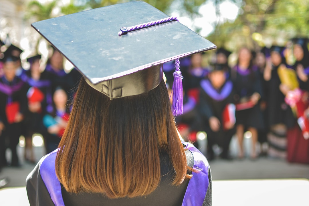 Studentessa con toga e cappello di laurea in primo piano, gruppo di laureati sfocati sullo sfondo, simbolo di ammissione alla maturità