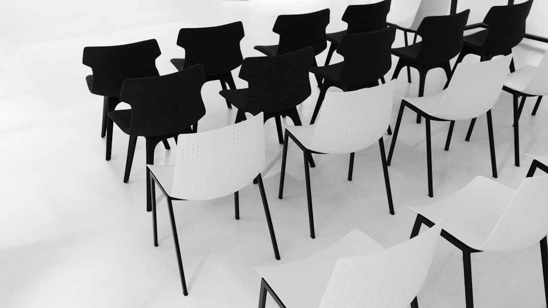 File di sedie bianche e nere in una sala, metafora per la gestione del personale scolastico e la copertura dei posti vacanti.