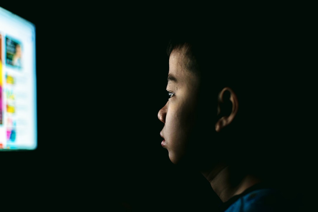 Bambino guarda schermo illuminato al buio, riflessione sull'impatto dell'IA e del controllo tecnologico sui minori e sul loro futuro.