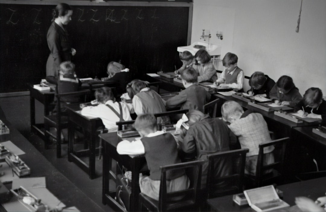 Fotografia in bianco e nero di una classe scolastica d'epoca con bambini che scrivono, riflettendo le sfide tra meritocrazia e disuguaglianze nell'istruzione.